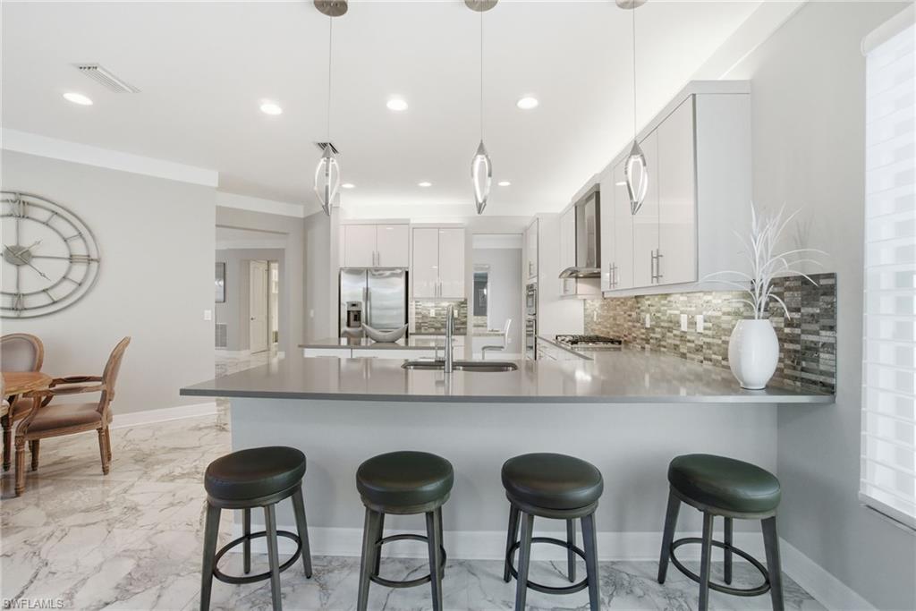 4654 Kensington Circle Naples, FL 34119 - Photo 11 of 48 a kitchen with stainless steel appliances granite countertop a dining table chairs and sink