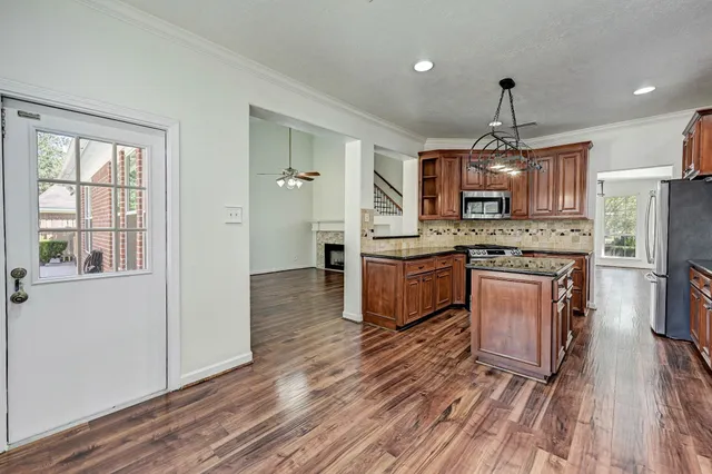 a kitchen with kitchen island granite countertop wooden floors stainless steel appliances a sink and a window