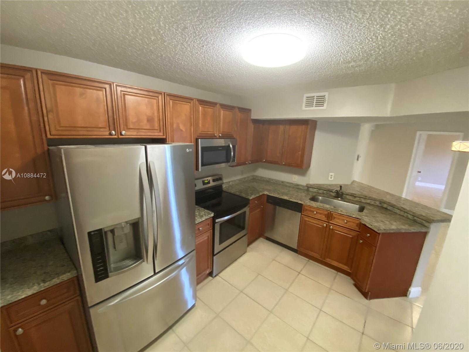 8741 Wiles Road, Unit 204 Coral Springs, FL 33067 - Photo 2 of 22 a kitchen with granite countertop a refrigerator and wooden cabinets