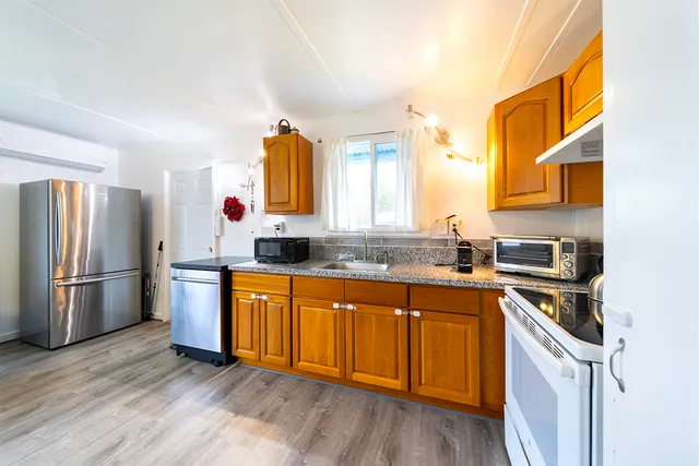 a kitchen with stainless steel appliances granite countertop a stove a sink dishwasher a refrigerator and wooden cabinets with wooden floor