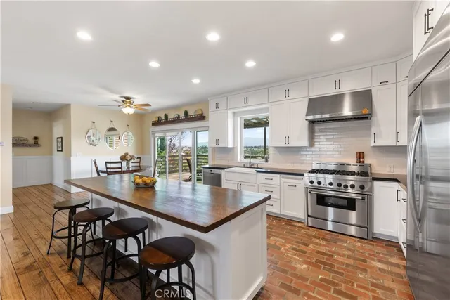 a living room with stainless steel appliances furniture wooden floor and a kitchen view