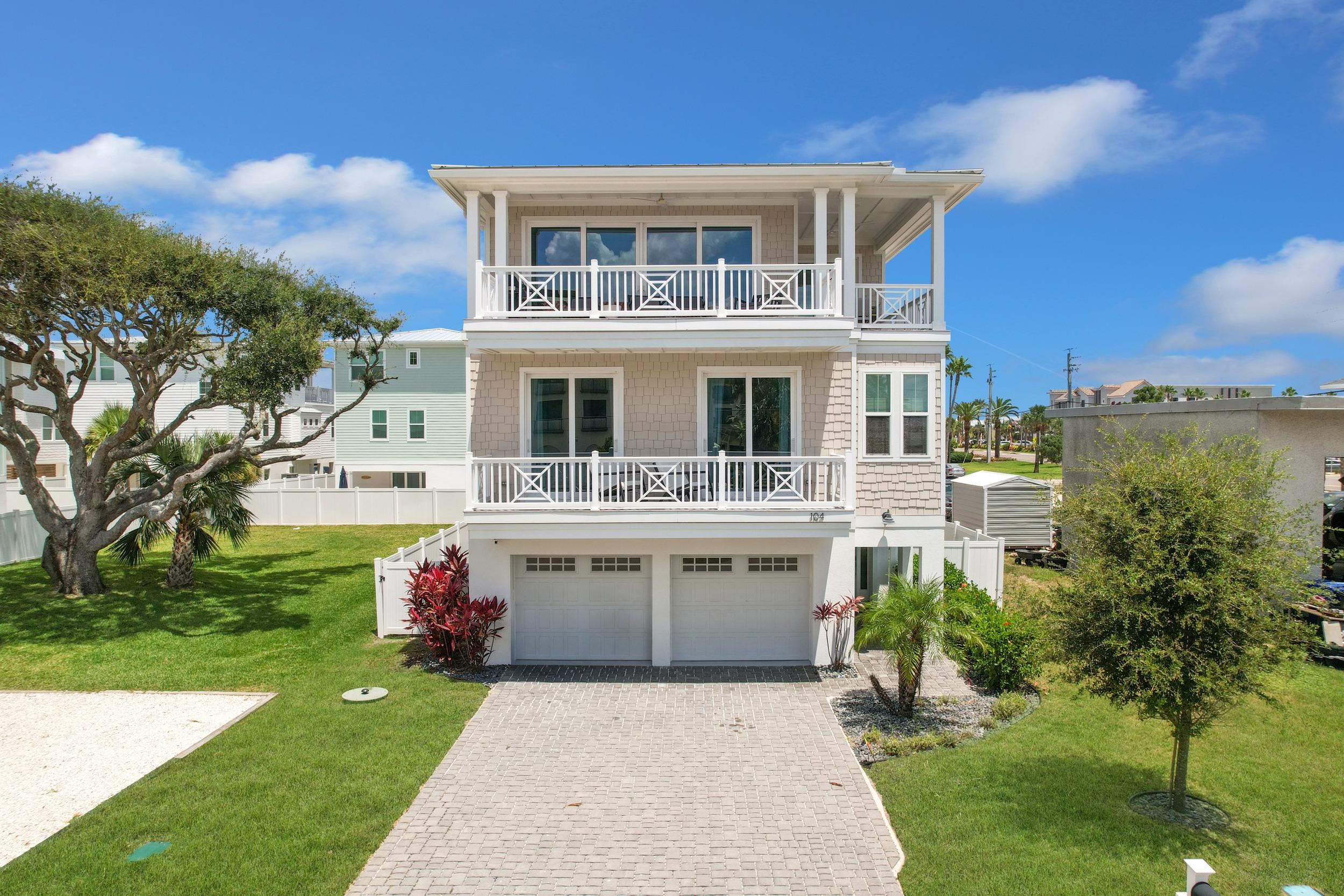 Raised beach house featuring a front yard, decorative driveway, a garage, and a balcony