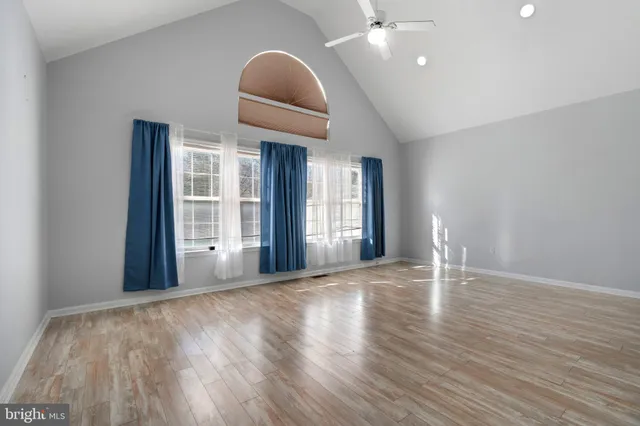 a view of an empty room with wooden floor and fan