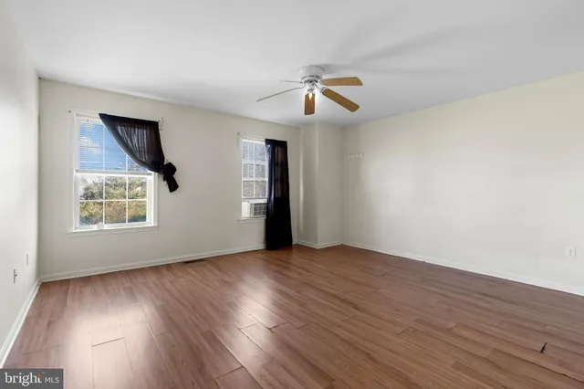 an empty room with wooden floor chandelier fan and windows
