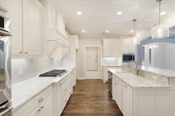 a large white kitchen with stainless steel appliances granite countertop a stove oven a sink dishwasher and a refrigerator with wooden floor