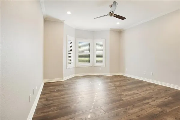 an empty room with wooden floor ceiling fan and windows