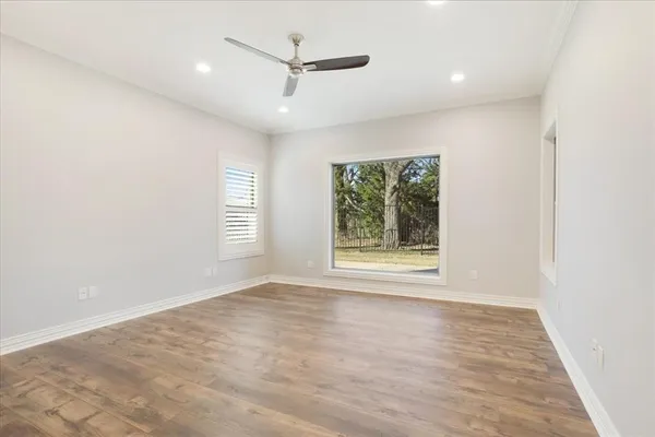 an empty room with wooden floor ceiling fan and windows