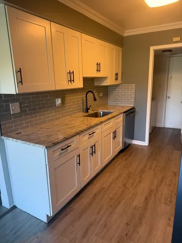 a kitchen with stainless steel appliances granite countertop a sink a stove and white cabinets with wooden floor