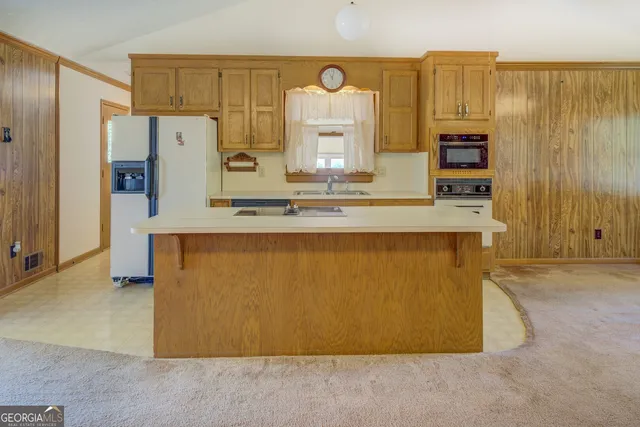 a room with kitchen island a counter top space a sink a refrigerator and cabinets