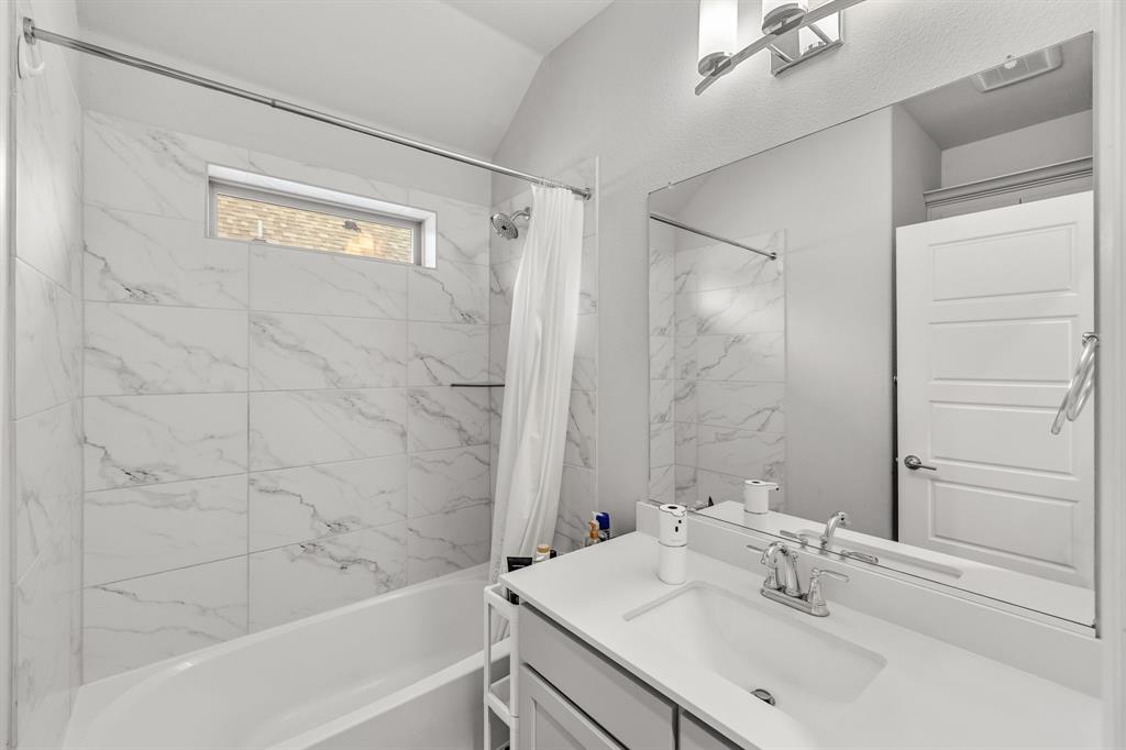 7852 Buffaloberry Road Frisco, TX 75035 - Photo 25 of 36 Bathroom featuring a spacious tub with marble-look tile surround, an elongated transom window, a single vanity with a white countertop and integrated sink, and an expansive wall mirror