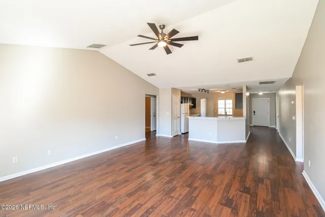 a view of an empty room with wooden floor and a ceiling fan