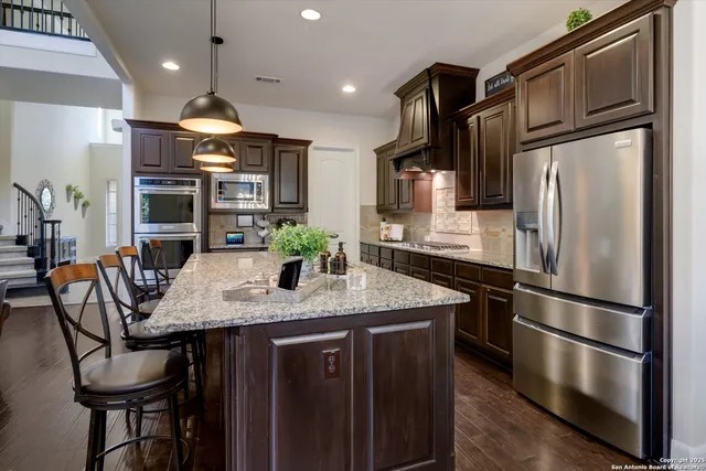 a kitchen with stainless steel appliances granite countertop a refrigerator a stove a kitchen island a dining table and chairs