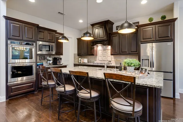 a kitchen with stainless steel appliances granite countertop a stove a refrigerator a kitchen island a table and chairs