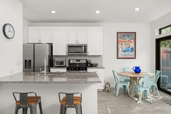 a kitchen with stainless steel appliances granite countertop a dining table chairs refrigerator and sink