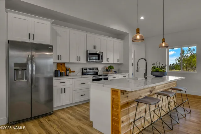 a kitchen with stainless steel appliances granite countertop a refrigerator a sink dishwasher a stove and white cabinets with wooden floor