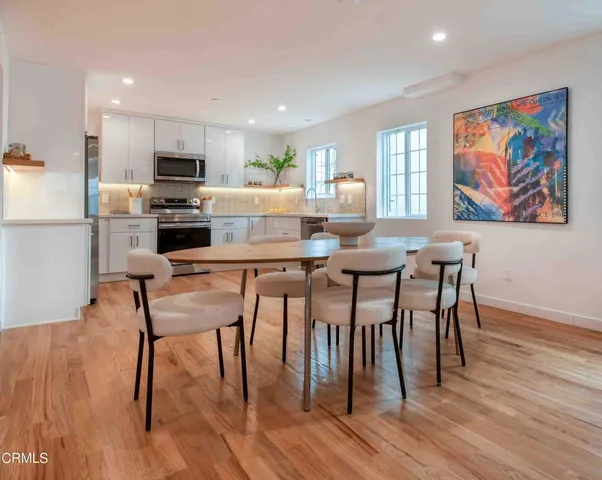 a kitchen with stainless steel appliances kitchen island granite countertop a dining table chairs and a refrigerator