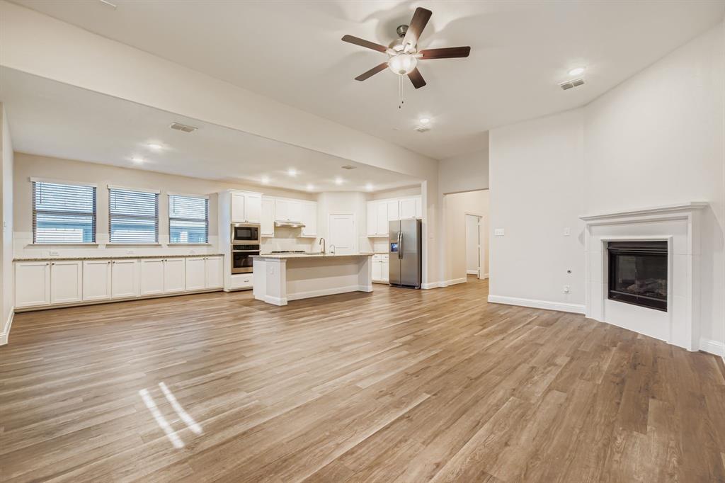 312 Magnolia Drive Oak Point, TX 75068 - Photo 5 of 28 Unfurnished living room with light wood-style floors, a ceiling fan, a glass covered fireplace, and recessed lighting