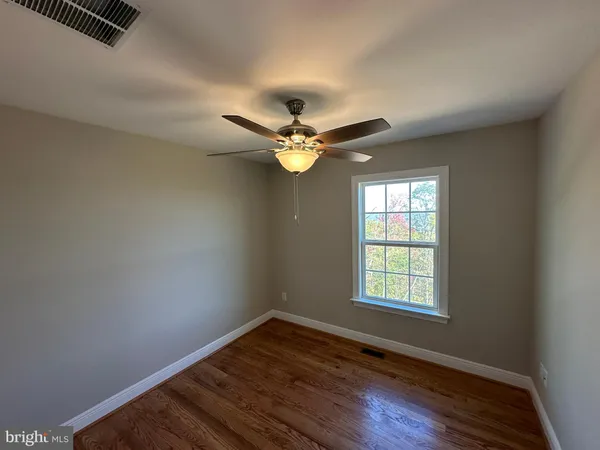 an empty room with wooden floor fan and windows