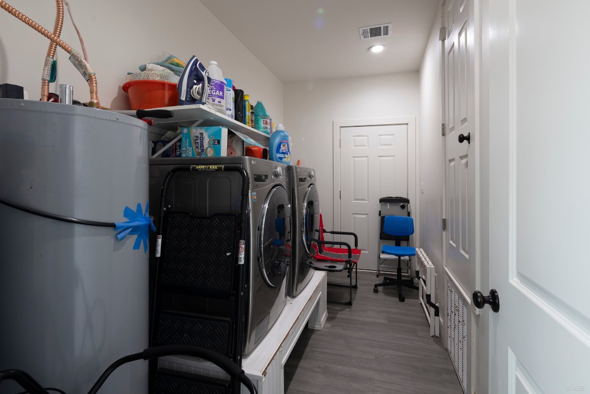 135 Wilbarger Bend Road Bastrop, TX 78602 - Photo 15 of 37 Clothes washing area featuring visible vents, wood finished floors, washing machine and clothes dryer, laundry area, and water heater