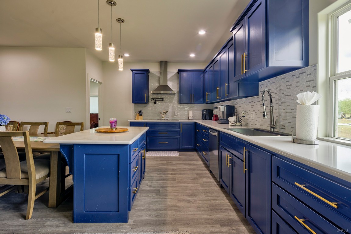 135 Wilbarger Bend Road Bastrop, TX 78602 - Photo 4 of 37 Kitchen with a sink, wall chimney range hood, tasteful backsplash, blue cabinets, and light countertops
