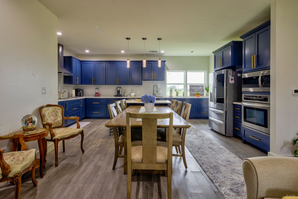 135 Wilbarger Bend Road Bastrop, TX 78602 - Photo 5 of 37 Kitchen featuring wall chimney range hood, stainless steel appliances, decorative backsplash, and blue cabinetry
