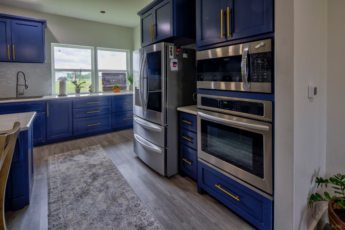135 Wilbarger Bend Road Bastrop, TX 78602 - Photo 8 of 37 Kitchen featuring a sink, wood finished floors, blue cabinets, decorative backsplash, and appliances with stainless steel finishes