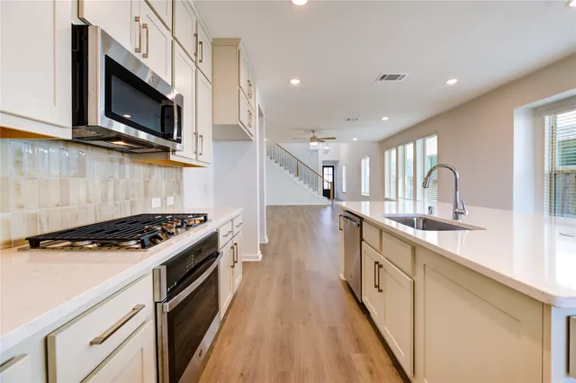 a kitchen with stainless steel appliances a sink dishwasher a stove top oven a refrigerator with wooden floor