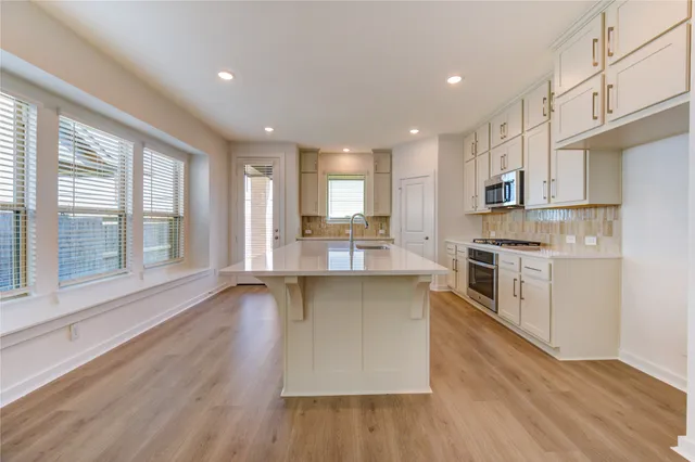 a kitchen with stainless steel appliances a stove top oven a sink a refrigerator white cabinets and wooden floor