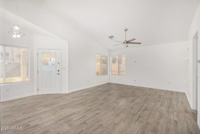 an empty room with wooden floor ceiling fan and windows