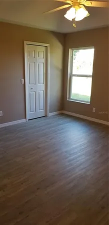 an empty room with wooden floor chandelier fan and windows