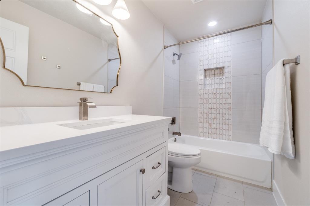 7115 Meadow Road Dallas, TX 75230 - Photo 17 of 22 Bathroom featuring a white vanity with a white countertop, a decorative mirror with a gold-toned frame, and a white bathtub with tile surround