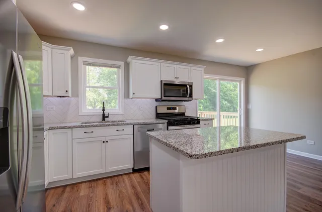 a kitchen with stainless steel appliances granite countertop a sink a stove a refrigerator cabinets and a window