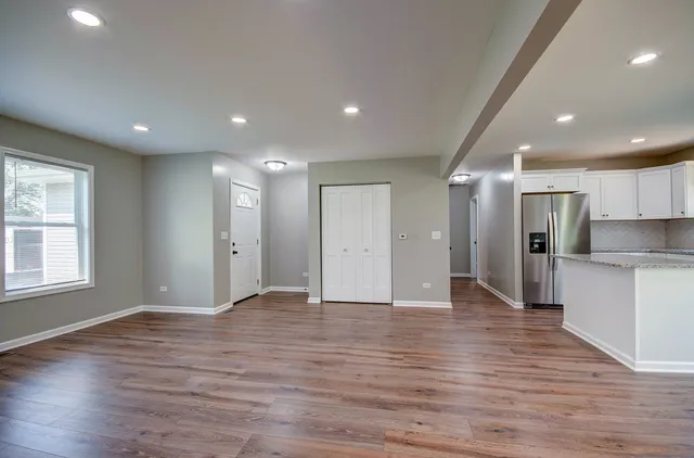 a view of an empty room with wooden floor and a kitchen