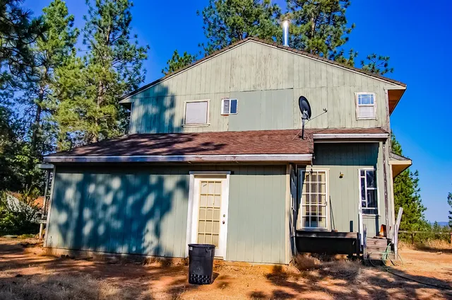 a view of a white house with a small yard plants and large tree