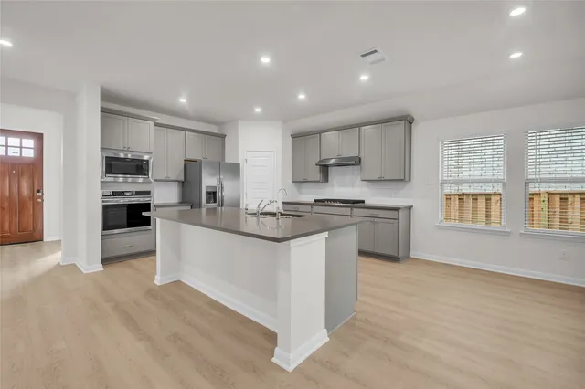 a kitchen with stainless steel appliances granite countertop a sink a stove a refrigerator and white cabinets with wooden floor