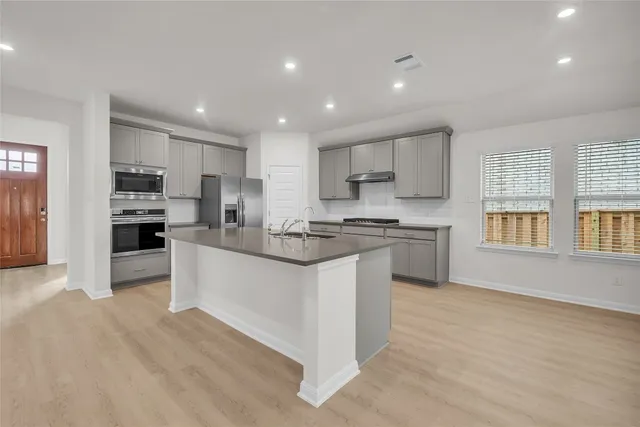 a kitchen with stainless steel appliances granite countertop a sink a stove a refrigerator and white cabinets with wooden floor