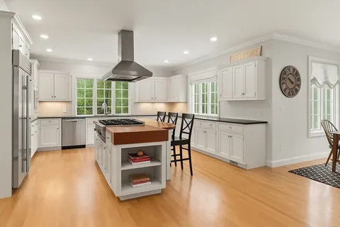 a kitchen with kitchen island granite countertop a stove a sink a refrigerator and white cabinets with wooden floor