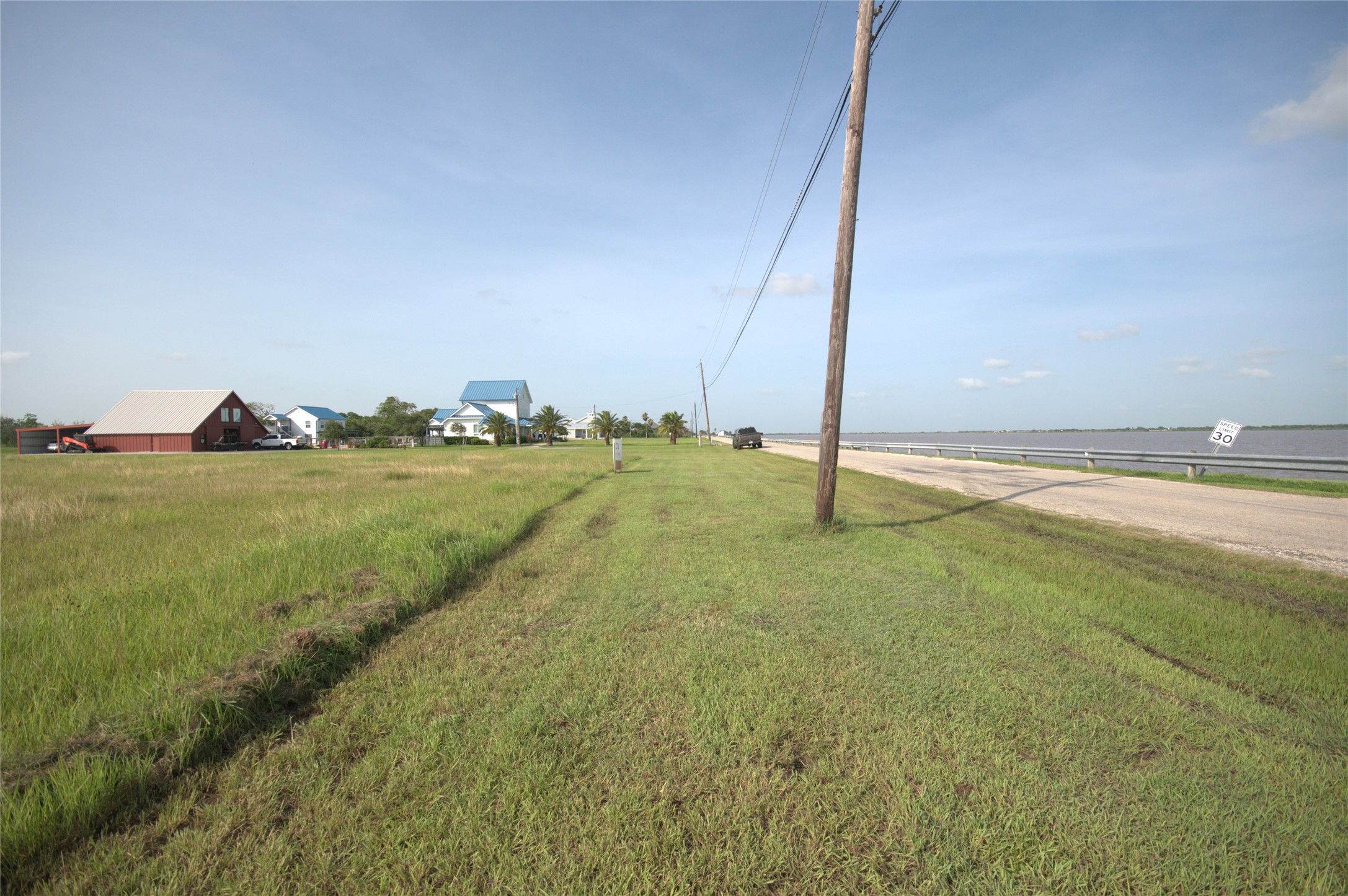 305 Bayshore Road Palacios, TX 77465 - Photo 14 of 25 Green expanse bordering a tranquil water body, with a red barn-style structure and other homes in the distance.