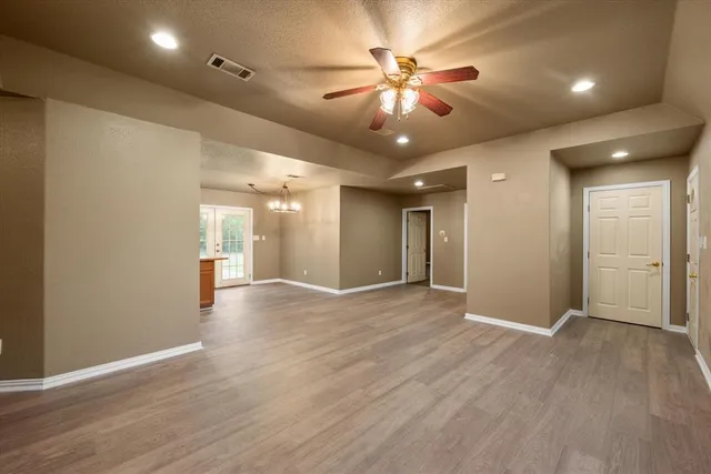 a view of an empty room with wooden floor and a ceiling fan