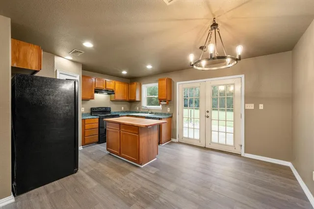 a large kitchen with stainless steel appliances granite countertop a refrigerator a sink dishwasher a stove and a dining table with wooden floor