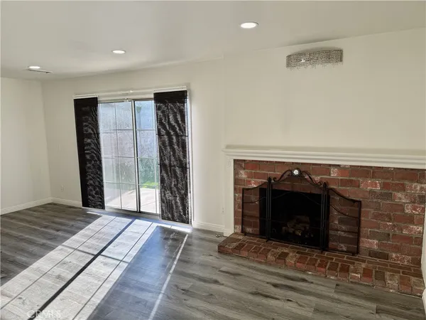 a view of an empty room with wooden floor fireplace and a window