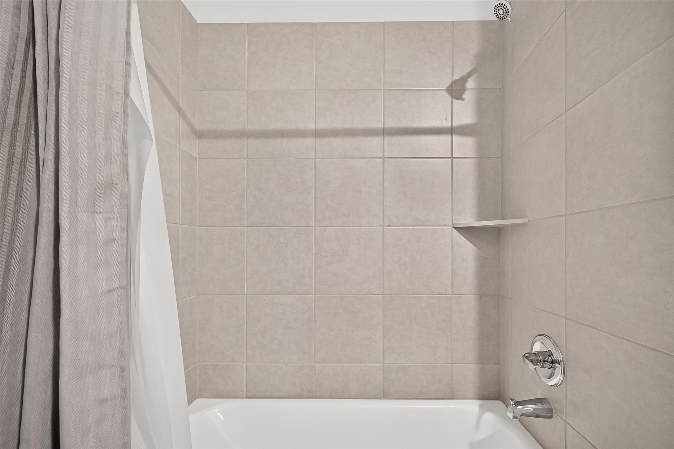4004 Baja Lane Houston, TX 77045 - Photo 29 of 34 This stylish shared bath showcases an immaculate tub-shower setup accented by classic chrome fixtures and neutral tiled walls. A built-in corner ledge adds a touch of modern functionality to this bright, low-maintenance space.