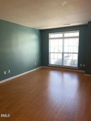 an empty room with wooden floor and windows with curtains