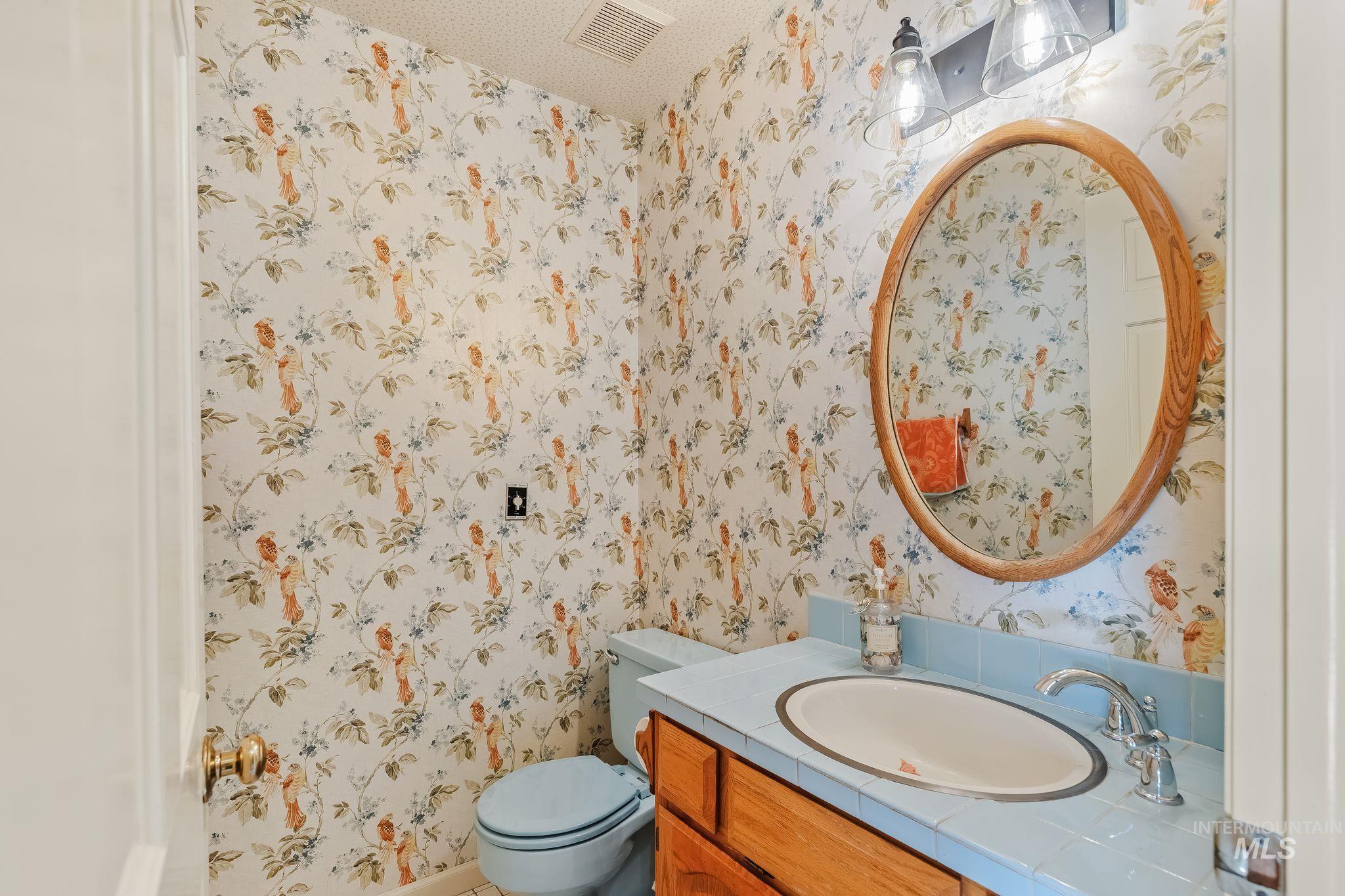 531 Silcott Road Clarkston, WA 99403 - Photo 15 of 43 Pedestal sink with chrome faucet, oval mirror with wood-finish frame, and floral pattern wallpaper