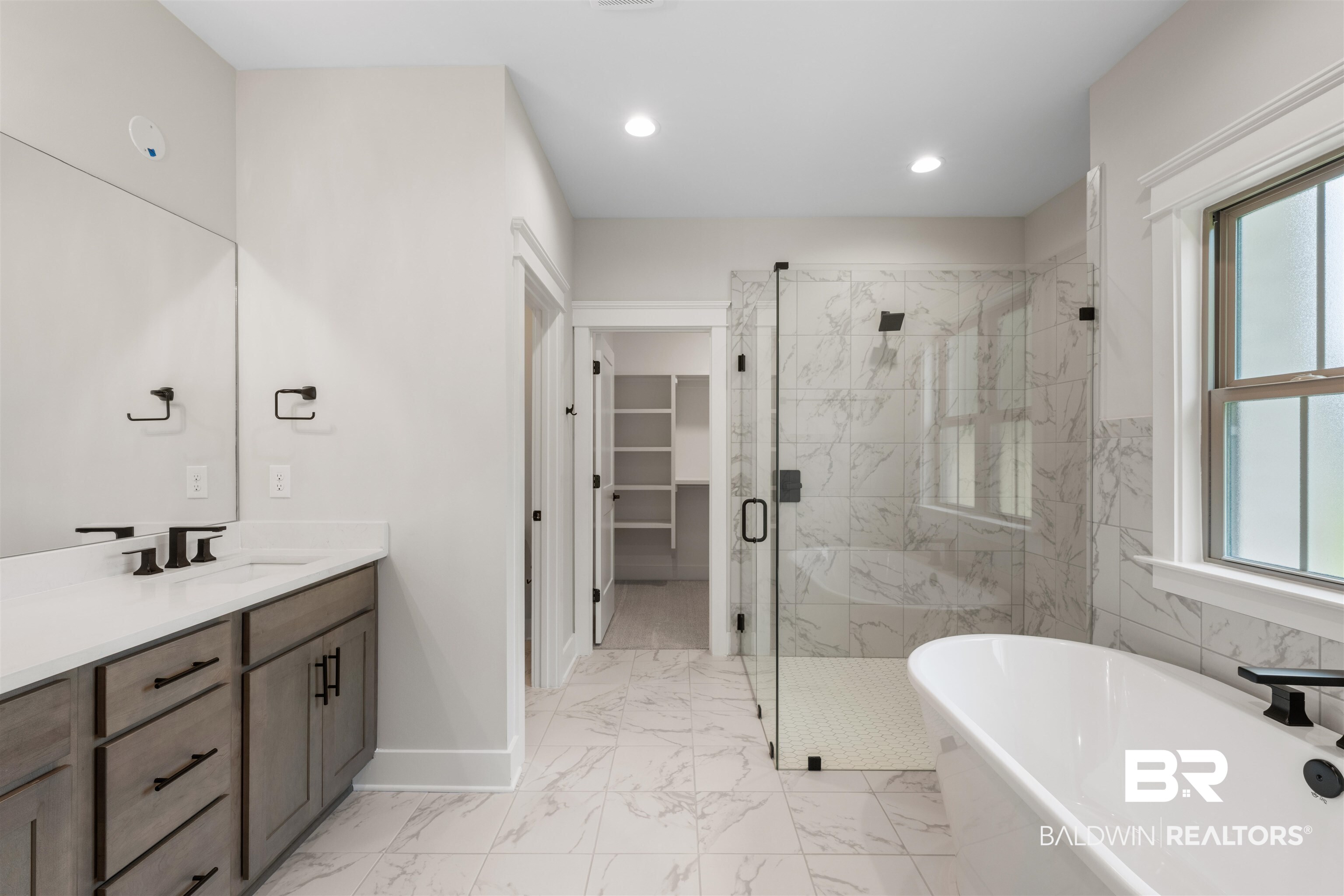 27494 Patch Pl Loop Daphne, AL 36526 - Photo 15 of 26 Spacious bathroom featuring a freestanding soaking tub, a walk-in shower with clear glass enclosure and tile surround, a double vanity with stone countertop and matte black fixtures, and marble-look tile flooring