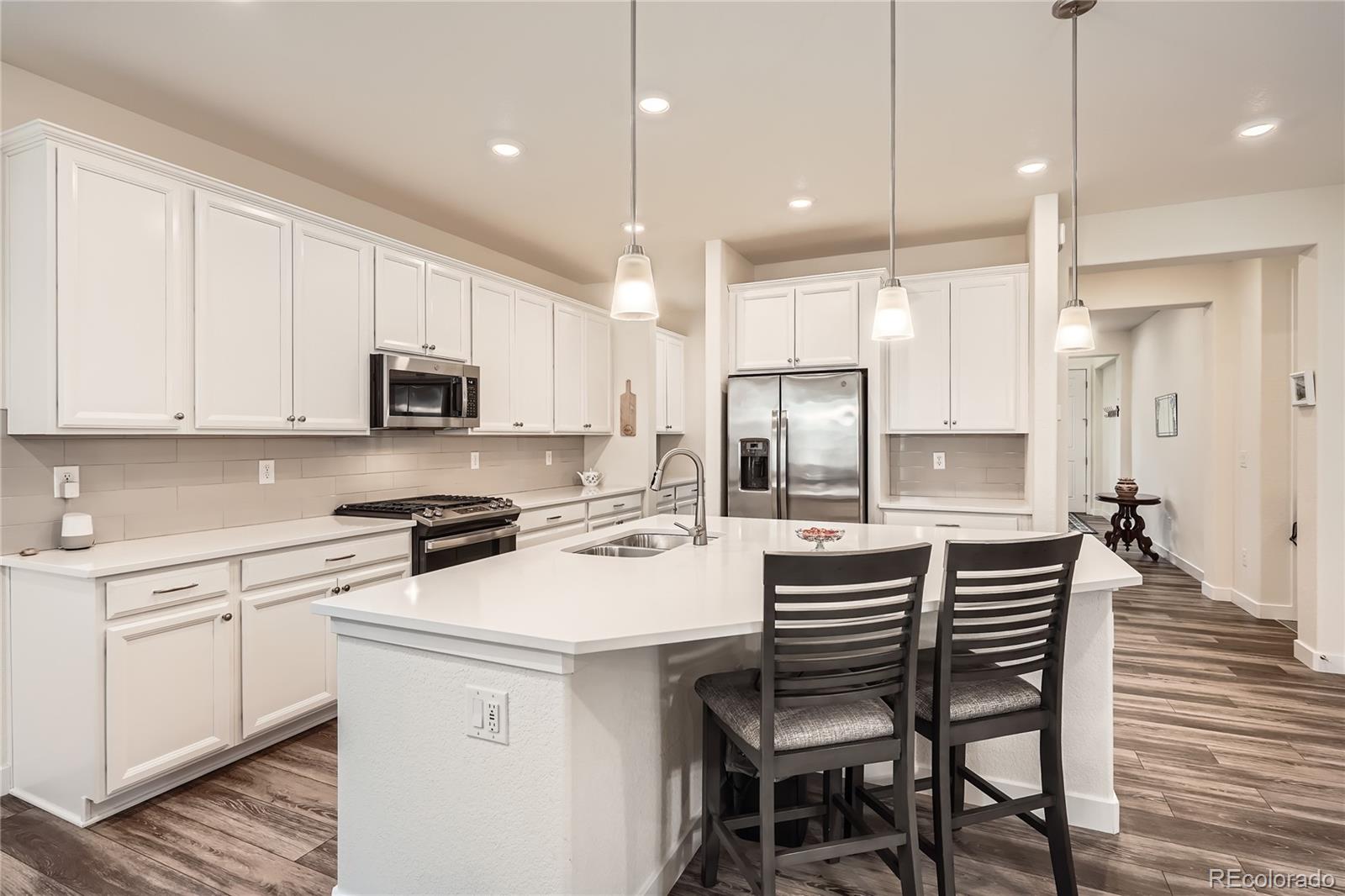 946 Compass Drive Erie, CO 80516 - Photo 6 of 28 a kitchen with stainless steel appliances a stove a sink a refrigerator white cabinets and chairs