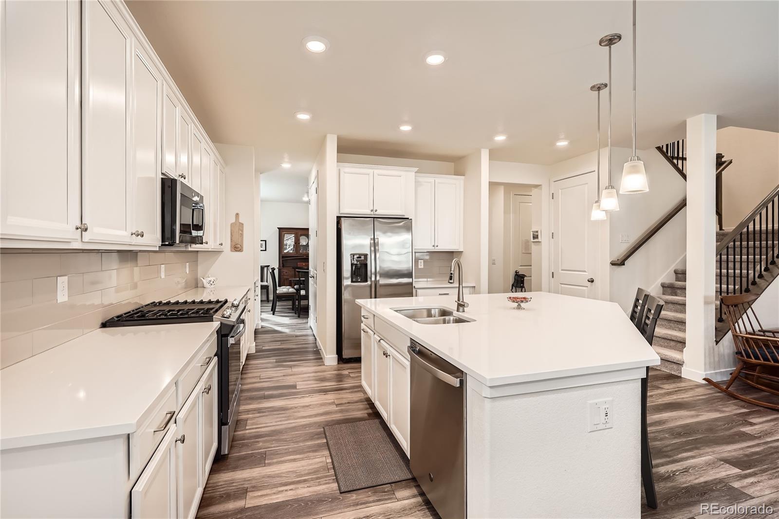 946 Compass Drive Erie, CO 80516 - Photo 7 of 28 a open kitchen with stainless steel appliances kitchen island a stove a sink a oven a refrigerator and white cabinets with wooden floor