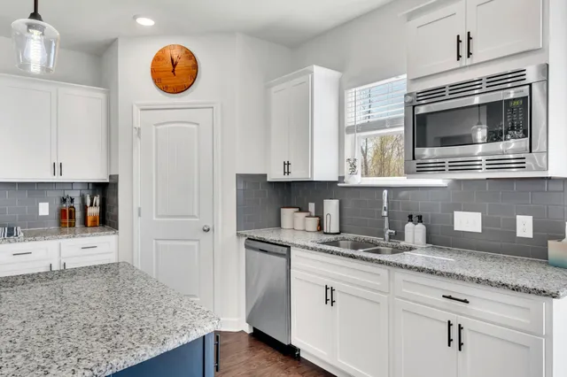 a kitchen with stainless steel appliances granite countertop a sink a stove oven and white cabinets with wooden floor