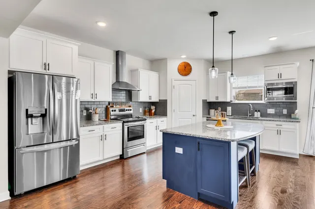 a kitchen with kitchen island granite countertop stainless steel appliances cabinets a sink and a wooden floor