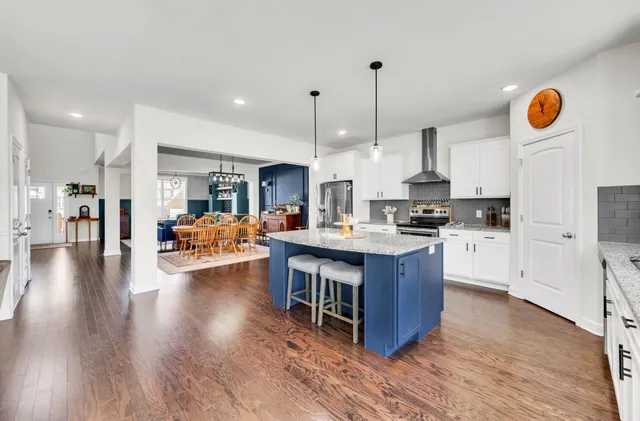 a open kitchen with stainless steel appliances granite countertop a stove top oven a refrigerator a kitchen island and couches with wooden floor